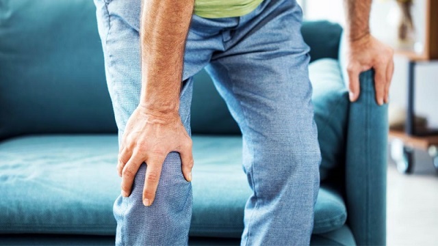 Người lớn tuổi ngồi trên giường buổi sáng, tay ôm khớp gối vì kêu lục cục